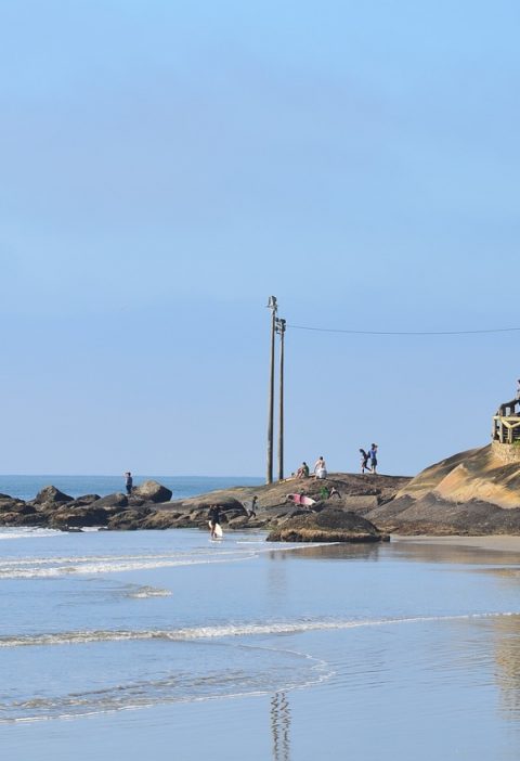 Praia de Matinhos litoral do paraná, com uma casa, pedra e sufistas ao fundo
