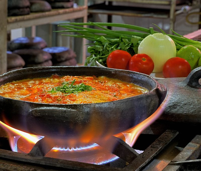 Uma panela de ferro com moqueca capixaba dentro cozinhando no fogo alto