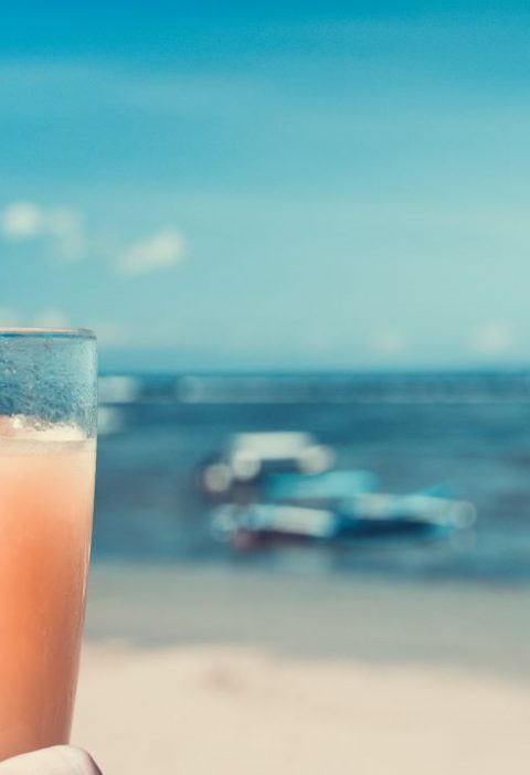 Foto da mão de uma pessoa segurando uma taça com bebidas típicas de praias