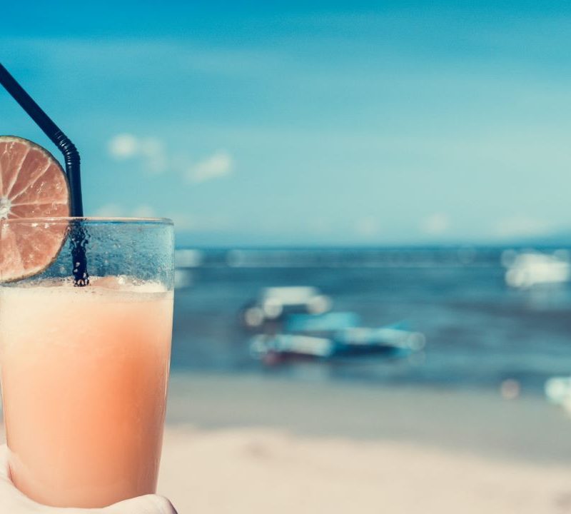 Foto da mão de uma pessoa segurando uma taça com bebidas típicas de praias